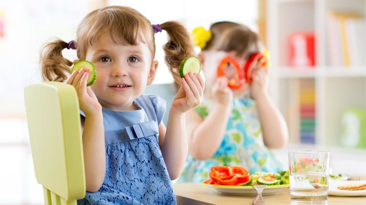 Preschool girls eating fresh food at table