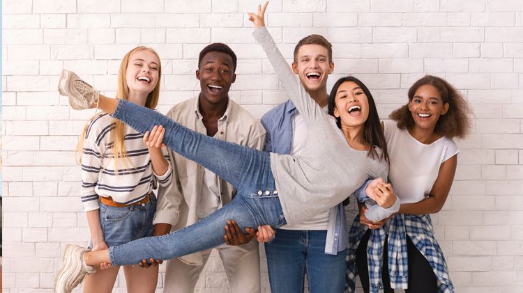 Joyful international group of students lifting Asian girl up, having fun over white wall background